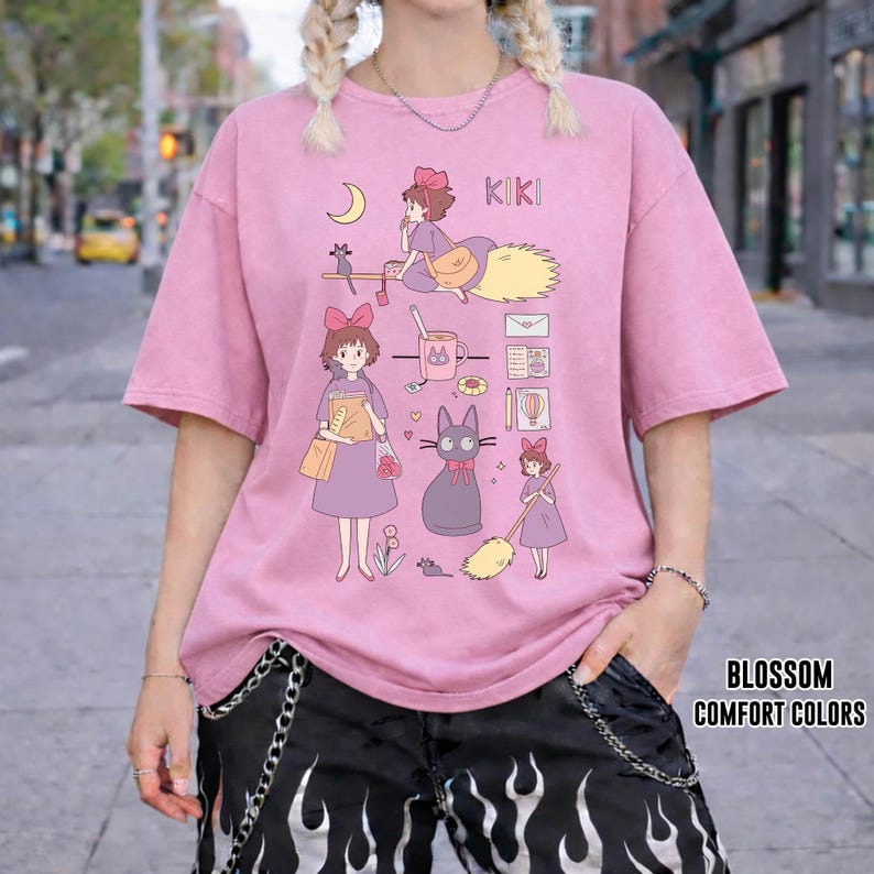 Peut inclure: T-shirt rose avec un dessin anim&eacute; repr&eacute;sentant une fille sur un balai, un chat noir et d'autres illustrations. Le mot "KIKI" est imprim&eacute; en haut. Le texte "BLOSSOM COMFORT COLORS" est imprim&eacute; en bas &agrave; droite.