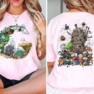 Op de afbeelding: Lichtroze t-shirt met een kleurrijk grafisch ontwerp uit een populaire animatiefilm. Het ontwerp aan de voorkant is een cirkelvormige opstelling van personages en landschappen. De achterkant van het shirt toont een gedetailleerde illustratie van een kasteel en verschillende personages.