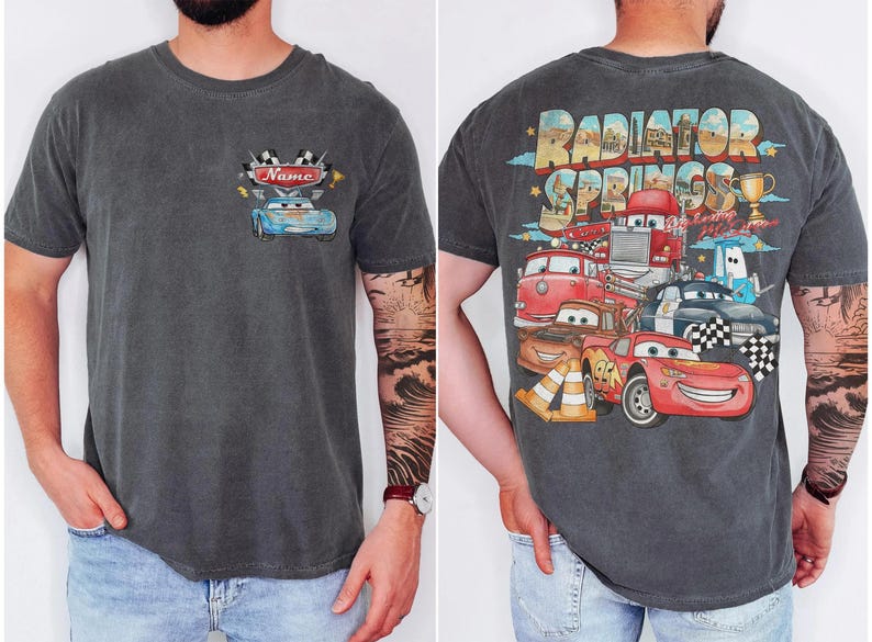 May include: Dark grey t-shirt with a front and back design. The front features a blue car graphic with the word "Name" and racing flags. The back displays a colourful graphic of cartoon cars with the words "Radiator Springs".