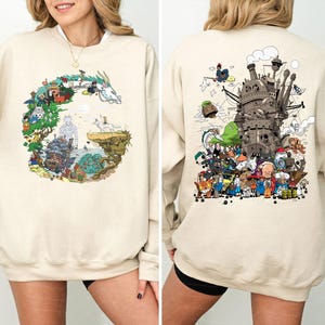 Op de afbeelding: Beige sweatshirt met kleurrijke illustraties uit een populaire animatiefilm. Het ontwerp aan de voorkant is een cirkelvormige opstelling van personages en landschappen. De achterkant van de sweatshirt toont een gedetailleerde afbeelding van een kasteel en meer personages.
