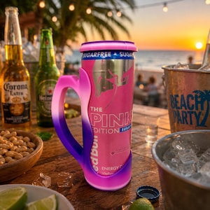 May include: A pink and purple gradient handle sleeve holding a Red Bull The Pink Edition Sugarfree energy drink can. The can features a silver metallic finish with pink branding, text reading The Pink Edition Sugarfree, and a stylised bull graphic.
