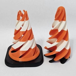 Peut inclure: Deux sculptures coniques abstraites. L'une est sur une base carrée noire, l'autre est autonome. Les deux présentent un motif en spirale avec des rayures orange et blanches alternées. Les sculptures sont sur fond blanc.