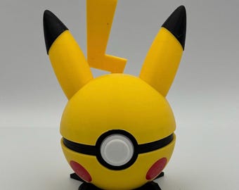 May include: A yellow and black Pikachu-themed Pokeball figure. The figure has a yellow body with black accents, red circles, and a white button. It features Pikachu's ears and a lightning bolt. The figure is on a black stand.