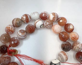 Op de afbeelding: Een ketting van edelsteen kralen in tinten bruin, wit en oranje. De kralen hebben een facet, getextureerd oppervlak en zijn geregen op een rood koord. De kralen zijn rond en variëren in grootte.