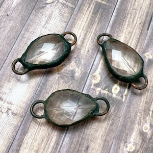 May include: Three clear glass beads with a faceted design, each encased in a dark green metal frame with two loops for attaching to jewelry or other crafts.