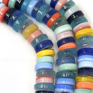 May include: Strands of colorful glass beads in various shades of blue, green, orange, yellow, and pink. The beads are round with a flat, disc-like shape, strung together on a clear cord. The beads are a mix of opaque and translucent.
