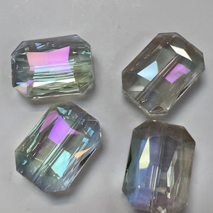 May include: Four clear, faceted crystal beads with iridescent color reflections. The beads are rectangular with cut corners, showcasing a range of colors including pink, purple, and green. These beads are suitable for jewelry making and crafts.