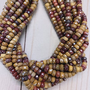 May include: A collection of faceted round beads in shades of mustard yellow, deep burgundy, and earthy brown, strung together on thin yellow thread. The beads have a polished, multi-faceted surface that reflects light, creating a textured appearance.