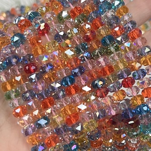 May include: A collection of multi-colored faceted crystal beads arranged in parallel vertical strands. The beads feature a variety of vibrant hues including red, orange, yellow, blue, green, and pink, each with a reflective surface and clear finish.