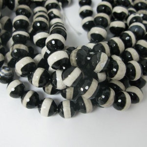 May include: A strand of black and white agate beads. The beads are round and have a faceted finish. The beads are strung on a clear thread.