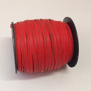 Op de afbeelding: Een spoel met rood lederen koord, gewikkeld om een zwarte kunststof spoel. Het koord is ongeveer 6 mm breed.