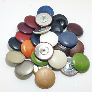 Peut inclure: Assortiment de boutons recouverts de cuir de différentes couleurs avec des tiges métalliques. Les boutons sont dans différentes nuances de brun, rouge, bleu, vert et beige.