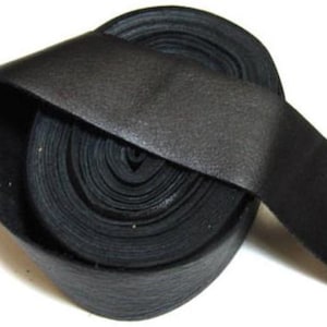 May include: A continuous roll of black leather strip material coiled into a circular shape. The leather has a smooth, matte surface texture and a consistent dark black color throughout the entire length of the coiled strip, showing a flat profile.