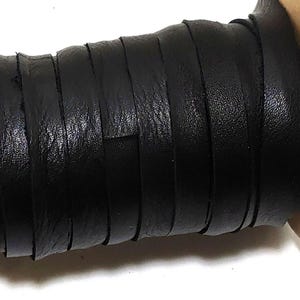 May include: A spool of black leather cord wrapped around a cylindrical cardboard core. The cord has a smooth, matte texture and is wound tightly in multiple parallel rows across the length of the spool, showing a consistent dark finish.