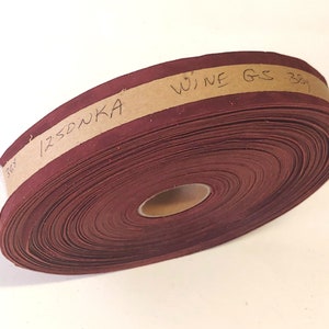 Op de afbeelding: Een rol maronkleurig lint van stof met een bruin papieren label met de tekst "WINE G-S 38" en "12SDNKA".