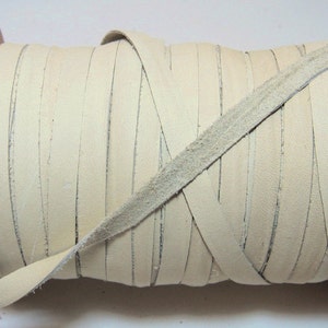 Może przedstawiać: Szpula z kremowym sznurkiem skórzanym. Sznurek jest ciasno nawinięty na drewnianej szpulce.