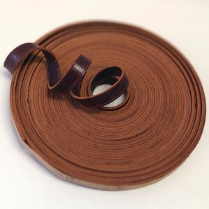 May include: A roll of brown leather cord, coiled and tied in a loop. The cord is approximately 1/2 inch wide.