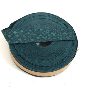 May include: A roll of dark green leather with a scale pattern. The leather is rolled up and tied with a brown ribbon.