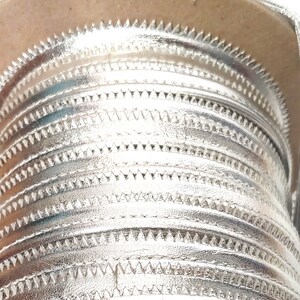 May include: A roll of silver metallic trim with a scalloped edge. The trim is wound around a cardboard spool.