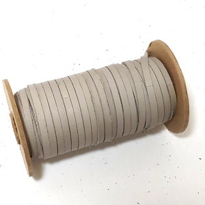 Puede incluir: Un carrete de cordón de cuero gris claro envuelto alrededor de un núcleo de cartón.