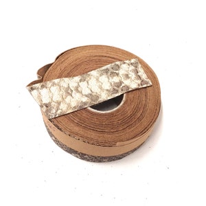 Op de afbeelding: Een rol bruin lederen koord met een stuk gepatenteerd leer erop. Het koord is om een kartonnen kern gewikkeld.