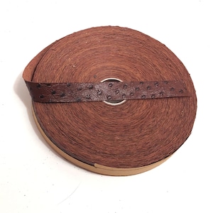 Może przedstawiać: Rolka brązowego sznurka skórzanego z owiniętą wokół niego brązową skórzaną taśmą z nadrukiem strusiego.