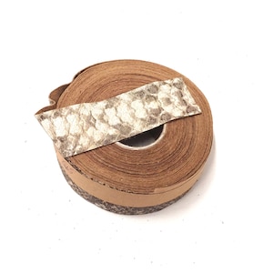 Może przedstawiać: Rolka brązowego sznurka skórzanego z kawałkiem wzorzystej skóry na górze. Sznurek jest owinięty wokół kartonowego rdzenia.