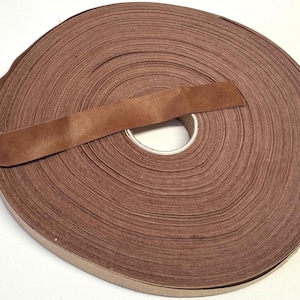 May include: A continuous roll of brown leather trim or binding tape wound into a tight circular spool. The material has a smooth, matte finish with a consistent medium brown color throughout the entire length of the coiled strip.