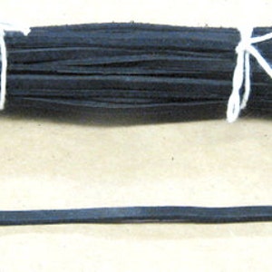 Puede incluir: Un paquete de tiras de cuero negro atadas con una cuerda blanca. Una sola tira de cuero negro se coloca debajo del paquete.