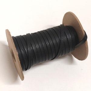 Puede incluir: Un carrete de cordón de cuero negro envuelto alrededor de un carrete de cartón.