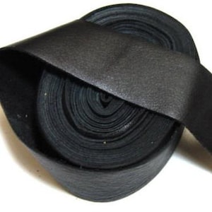 May include: A continuous roll of black leather strip featuring a smooth, matte surface texture. The material is coiled tightly into a circular shape, with one end of the strip extending outward to display the flat, flexible nature of the leather.