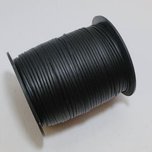 May include: A spool of black leather cord. The cord is wound tightly around a black plastic spool.