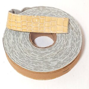 May include: A roll of light brown leather trim with a crocodile pattern. The trim is wrapped around a cardboard core.