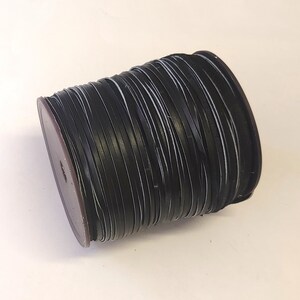 Może przedstawiać: Szpula czarnego sznurka skórzanego, ciasno nawinięta i gotowa do projektów rękodzielniczych.