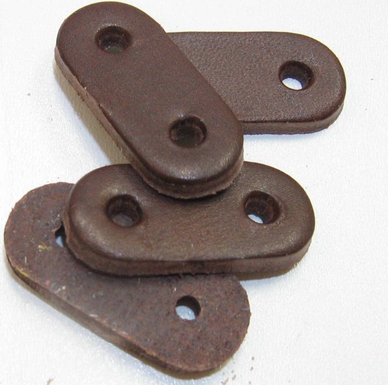 Puede incluir: Cuatro bucles de correa de cuero marr&oacute;n con dos agujeros cada uno. Los bucles son de forma ovalada y tienen una textura lisa y desgastada.