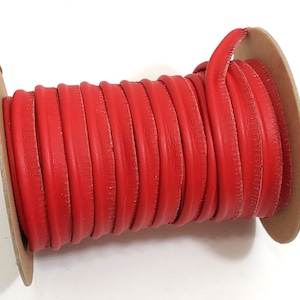 May include: A spool of bright red leather piping. The piping is tightly wound around a cardboard core. The leather has a smooth texture and a rounded edge. The image is shot against a white background.