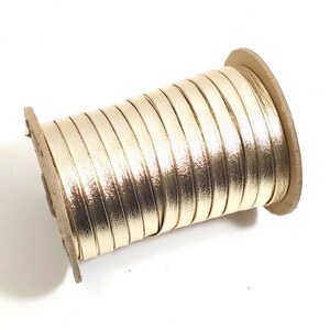 May include: A spool of gold metallic ribbon wound around a cardboard core. The ribbon is smooth and shiny.