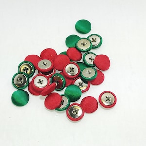 May include: A pile of red and green fabric covered buttons with silver metal centers.