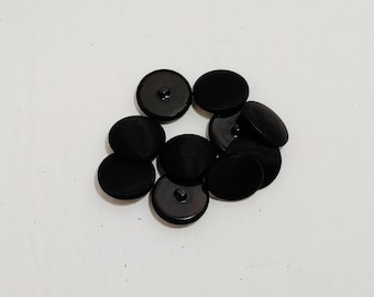Può includere: Un gruppo di dieci bottoni neri, alcuni con un centro rialzato e altri con una superficie piatta.