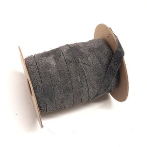 May include: A spool of gray suede leather cord wrapped around a cardboard spool.