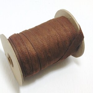 May include: A spool of brown suede ribbon wound around a cardboard spool.