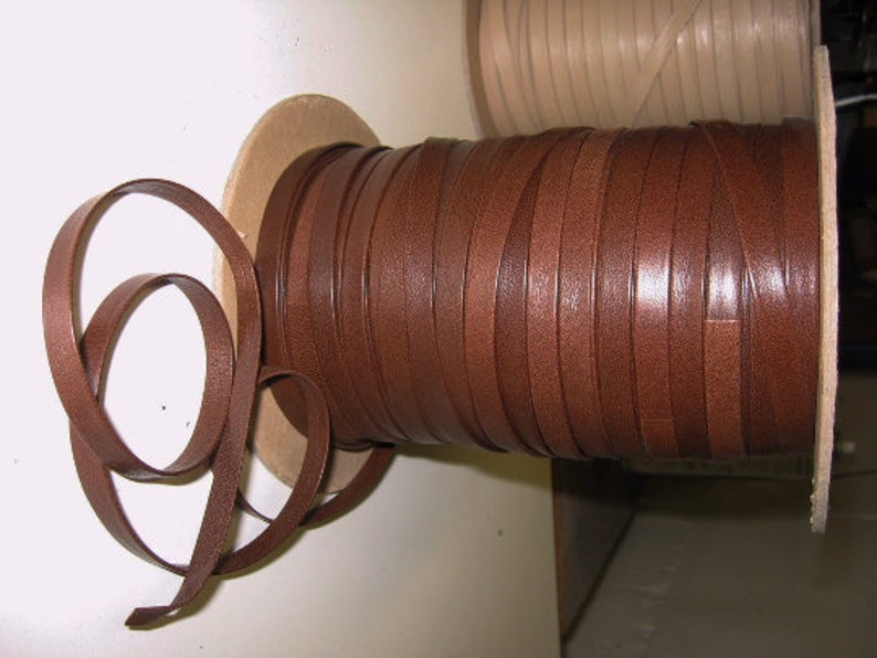 May include: A spool of brown leather cord, wound tightly and ready to be used for crafting projects. The cord is smooth and has a slight sheen.