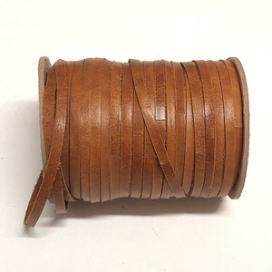May include: A roll of brown leather strips. The leather is a warm, medium brown colour with a slightly textured surface. The strips are tightly wound around a cardboard core, suitable for crafting or jewellery making.