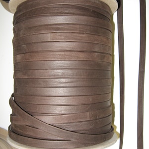May include: A spool of brown leather cord, wound tightly around a cardboard core. The cord is approximately 1/4 inch wide and has a smooth, polished finish.