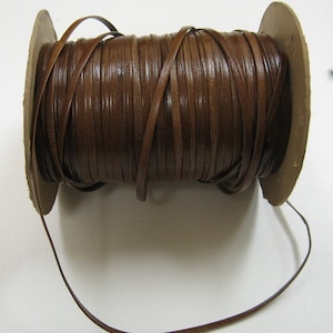 Könnte beinhalten: Eine Spule mit braunem Lederband, das um eine Pappspule gewickelt ist. Das Band ist etwa 6 mm breit und bereit für Bastelarbeiten.