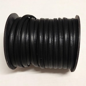 May include: A spool of black leather cord with a stitched edge. The cord is wound tightly around the spool.