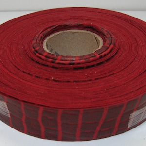 May include: A roll of red fabric tape with a black and white checkered pattern. The tape is wound around a cardboard core.