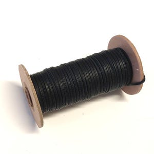 May include: A spool of black waxed cord wrapped around a cardboard spool.