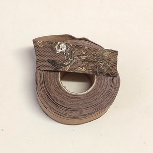 Może przedstawiać: Rolka brązowej i złotej wstążki z kwiatowym wzorem. Wstążka jest zwinięta, a koniec rolki jest widoczny.