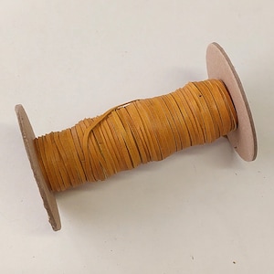 May include: A spool of tan leather cord wrapped around a cardboard spool.